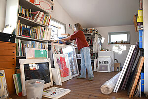 Tanja Zimmermann steht in ihrem Atelier. An der Wand stehen Regale und lehnen Kunstarbeiten.