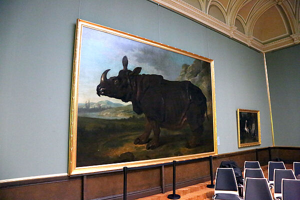 Ein Raum im Museum. An der Wand hängt ein großes Gemälde. Es zeigt ein Nashorn.
