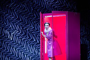 Eine Schauspielerin tritt aus einer roten Kabine und singt.