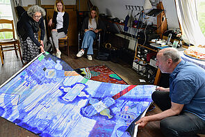 Die Kunstkommission im Atelier von Heinke Holm. Sie hocken vor einem großformatigen Bild auf der Erde.