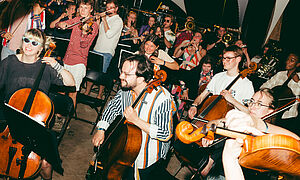 Junge Menschen spielen Instrumente, zum Beispiel Cello, Geige, Trompete, Tuba, Klarinette.