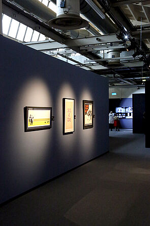 Blick in einen dunklen Raum. Die Bilder sind angestrahlt.