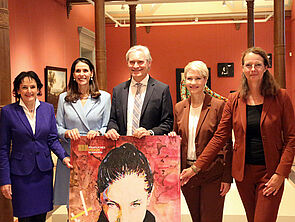 5 Personen stehen nebeneinander. Vor wirbt ein Plakat für das Staatliche Museum.