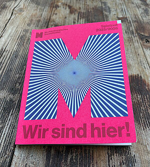 Ein Heft. Das Heft hat einen rosafarbenen Umschlag. Auf dem Umschlag ist ein großes M.