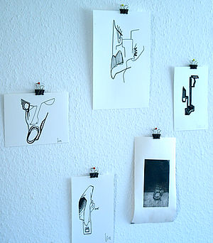 An einer Wand hängen fünf kleine Zeichnungen auf weißem Papier.