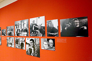 Porträts hängen an einer roten Wand.