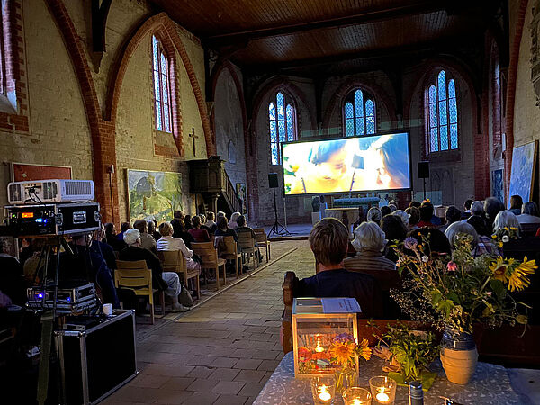 Ein Kirchensaal besetzt mit Menschen, die einen Film gucken.