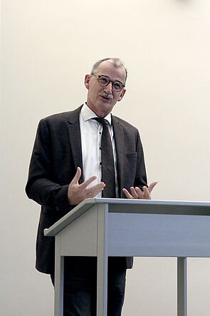 Ein Mann steht am Pult und spricht zu den Gästen.