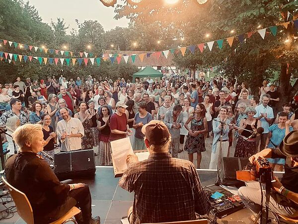 Fans stehen vor der Bühne, klatschen, tanzen. Auf der Bühne spielt eine Band.