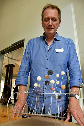 Ein Mann steht hinter seinem Kunstobjekt.