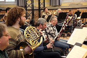 Musikerinnen und Musiker. Im Vordergrund wird ein Horn gespielt.