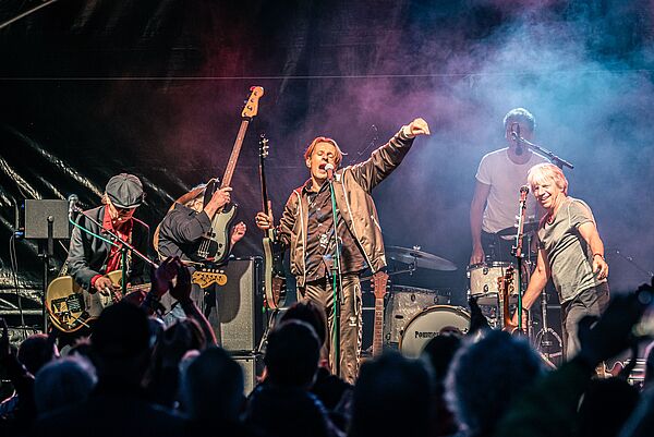 Alexander Scheer, Andreas Dresen & Band stehen vor Publikum auf einer Bühne und spielen ein Konzert.