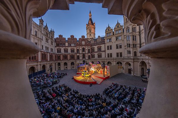 Im Innenhof des Schweriner Schlosses steht eine Bühne. Darauf findet eine Aufführung statt. Vor der Bühne sitzt Publikum.