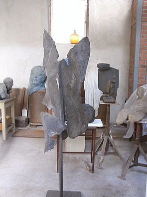 An einer Stange mit großem Standfuß hängt eine Skulptur.