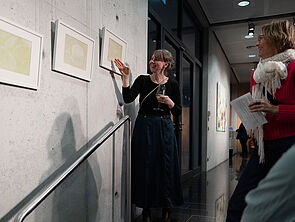 Eine Frau zeigt auf Bilder an einer Wand. Mehrere Leute hören ihr zu.