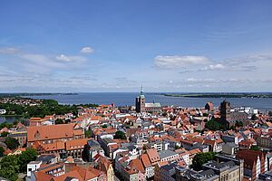 Eine Luftaufnahme der Stralsunder Innenstadt. Sie zeigt Dächer und Kirchen, Wasser und Bäume.  