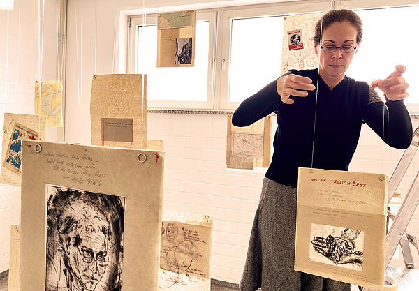 Karen Kunkel steht auf einer Leiter. Von der Decke hängen ihr Collagen aus Butterbrotpapier. Eine davon bringt sie in die richtige Position.