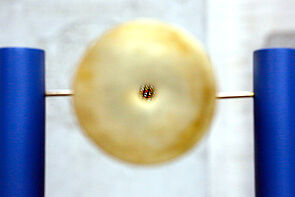 Ein goldenes, kreisförmiges Objekt. Gehalten von zwei blauen Ständern.