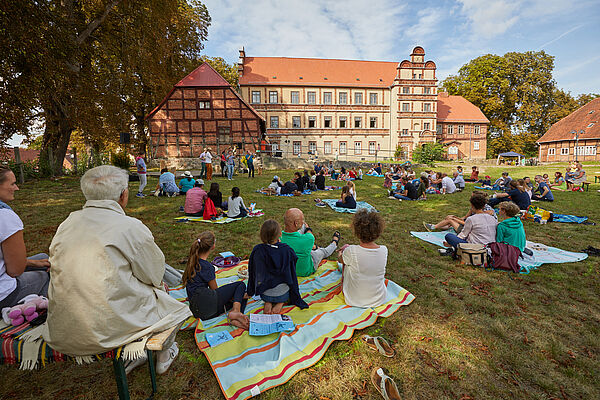 Familien sitzen auf einer Wiese vor dem Schloss auf Decken. 