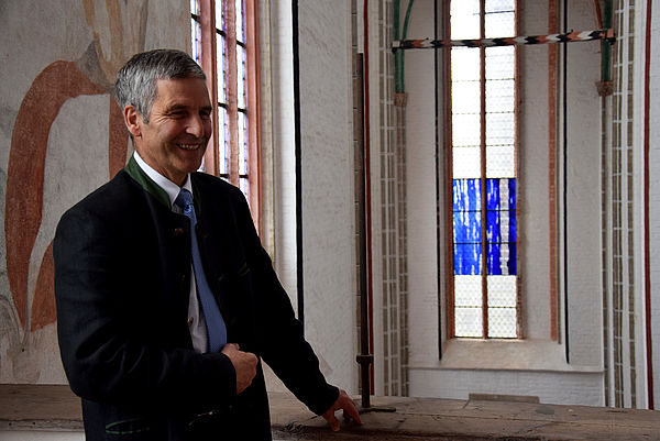 Domprediger Volker Mischok steht auf einer Empore. Im Hintergrund: Ein Kirchenfenster mit zwei blauen Glaselementen.