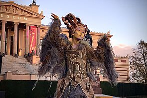 Eine Phantasiefigur tanzt auf einem Platz.