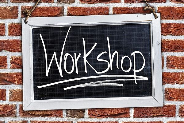 An einer Backsteinwand hängt eine Tafel. Auf der Tafel steht mit weißer Kreide das Wort Workshop.