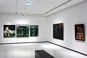 Blick in einen Ausstellungsraum. An den Wänden hängen fünf Bilder.
