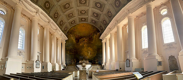 Der Innenraum der Kirche. Links und rechts stehen sechs weiße Säulen. Daneben sind die Fenster. Links und rechts stehen Kirchenbänke. In der Mitte ein Granitsarg. Am Ende des Raumes führen Treppen links und rechts zum Altar. Hinter dem Altar befindet sich das Wandbild. Am Altar stehen Kerzenleuchter und ein Kreuz.