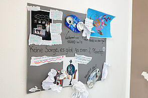 Eine Collage aus Texten, Bildern, Gegenständen. Alle sind auf graue Pappe geklebt.