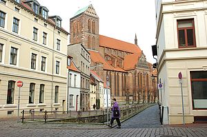 Die St.-Nikolai-Kirche in Wismar. Der Backsteinbau wird von beigefarbenen Häusern umrahmt.