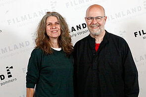 Ein Mann und eine Frau werden vor einer Festivalwand fotografiert.