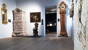 Möbel aus den letzten Jahrhunderten: ein Kachelofen, eine Uhr und Figuren.