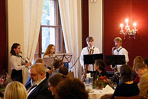 Vier junge Musiker spielen Saxophon. Im Vordergrund sitzen Gäste der Feier.