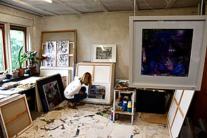 Eine Frau hockt in einem Atelier und betrachtet ein Bild.
