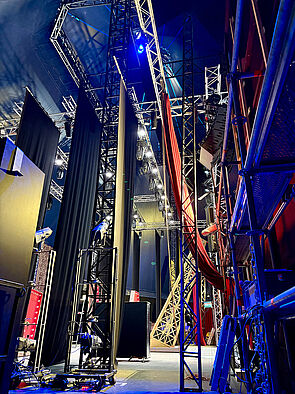 Von der Decke hängen Vorhänge. Auf dem Boden stehen Requisiten. Überall stehen Gerüste mit Technik. 