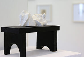 Eine weiße Figur liegt auf einem schwarzen Podest.