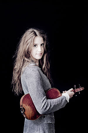 Vilde Frang steht vor einem dunklen Hintergrund und hält ihre Violine unter dem Arm.