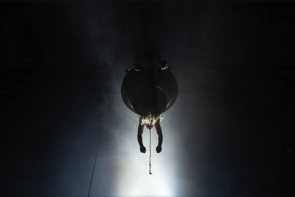 Ein dunkles Bühnenbild. Zwei Arme hängen aus einer Kugel an der Decke.