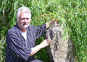 Prof. Wolfgang Vogt steht im Garten neben einer Skulptur.