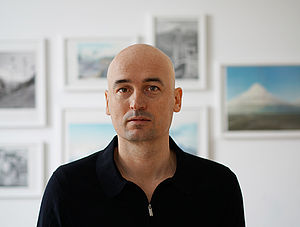 Ein Porträt von Alexander Glandien. Im Hintergrund hängen Bilder.