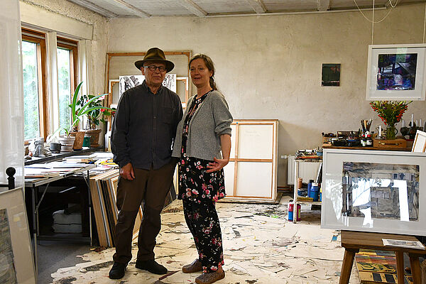 Ein Mann und eine Frau. Sie stehen einem Raum. An den Wänden lehnen große Bilder.