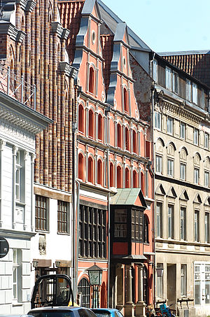 Ein weißes, ein rotes und ein cremefarbenes Giebelhaus. Dazwischen: ein Backsteinbau. Die Aufnahme stammt aus Stralsund.