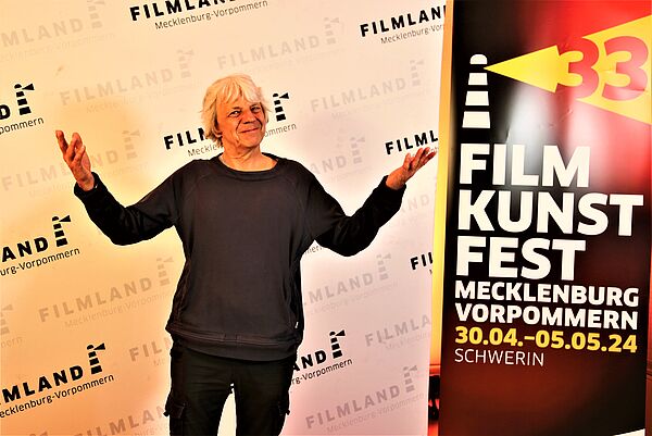 Ein Mann steht vor einem Plakat. Der Mann ist Andreas Dresen, ein Filmemacher.
