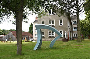 Eine große Skulptur steht auf einem Rasen vor einem großen Gebäude.