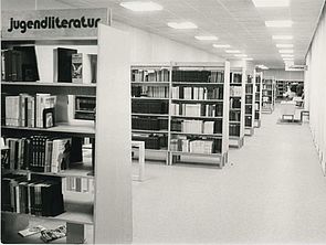 Ein Bibliotheksraum. Darin verteilen sich viele Bücherregale. Eine Schwarz-Weiß-Aufnahme.
