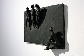 Skulpturen sind ausgestellt. Hier kleine Figuren. Eine schaut zu den anderen nach oben.