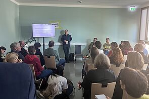 Teilnehmende sitzen in einem Seminarraum. Vorn spricht ein Dozent.