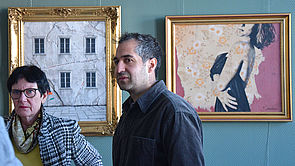 Zwei Menschen vor zwei Bildern an einer Wand.