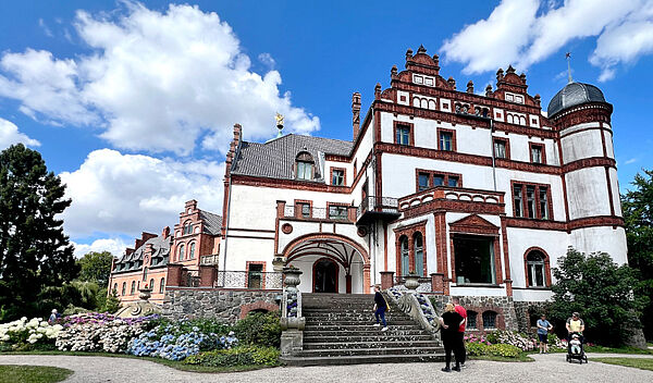 Ein Haus. Das Haus ist weiß. Der Eingang hat eine Treppe. Das Haus ist das Schloss Wiligrad.