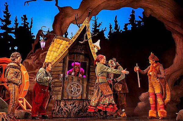 Eine Bühne. Auf der Bühne stehen Schauspieler. Das sind die Hexe Babajaga, Wassilissa und die verzauberten Söhne.